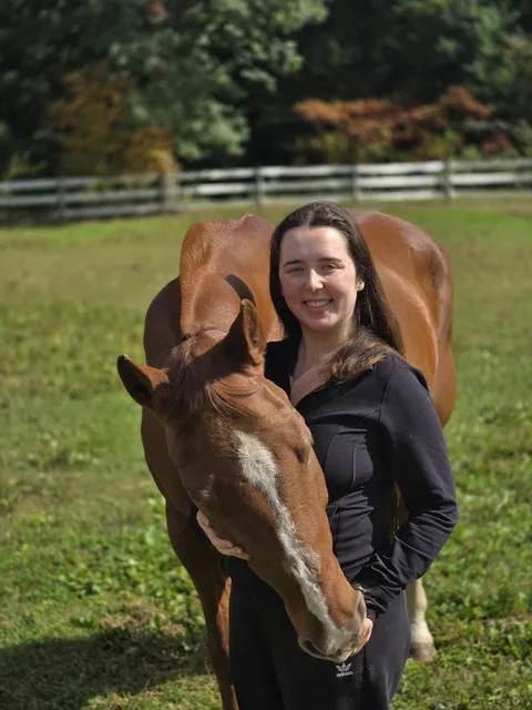 Ava standing beside a horse in a field