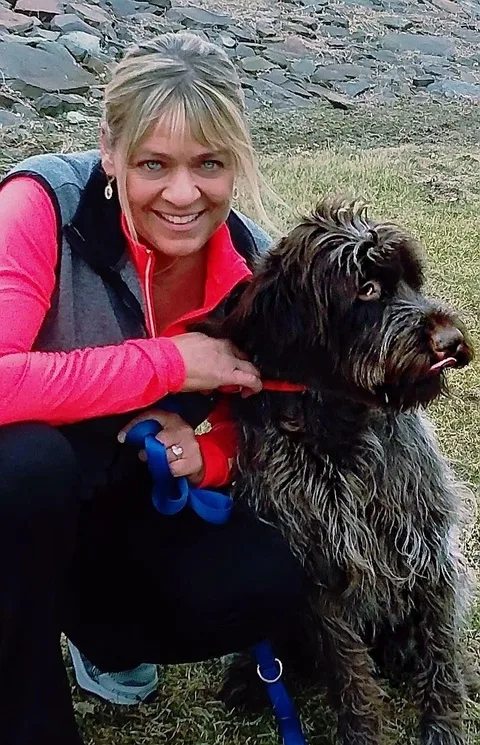 Cheryl crouching beside a dog outdoors