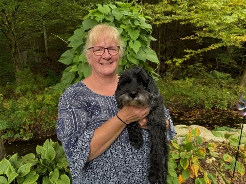 Diane holding a small black dog in a garden