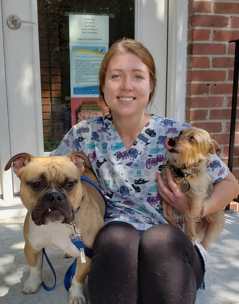 Emily, in scrubs, sitting on steps with two dogs